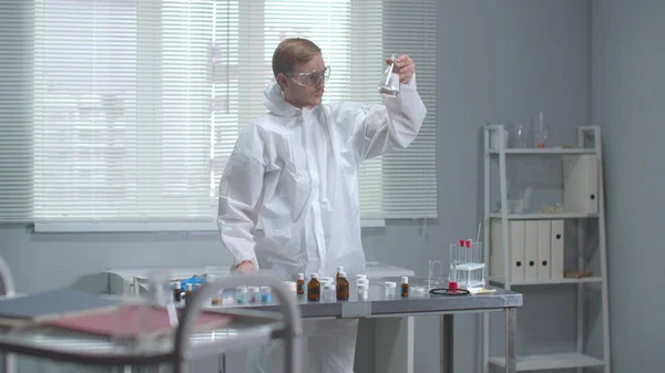 Человек в защитной рабочей одежде проверяет химическую пробирку в лаборатории — стоковое фото