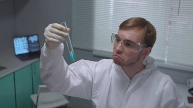 Koruyucu iş giysisinde mavi sıvıyla sallanan kimyager laboratuvarda bir şeyler söyle.