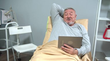 Adam hastanede yatağa uzanıp tabletten biriyle konuşuyor.