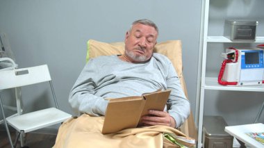 Adam hastanede yatağa uzanıp kitabı okumuş.