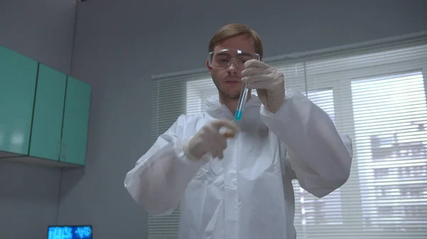 Химик в пробирке защитной рабочей одежды с голубой жидкостью и засорить ее в лаборатории — стоковое фото
