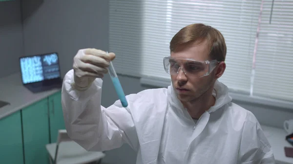 Chemist in protective workwear take tube with liquid and look disapproved in the laboratory — 스톡 사진