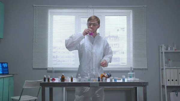 Вид спереди, человек в защитной рабочей одежде берет трубку с химикатом и нюхает ее в лаборатории — стоковое фото
