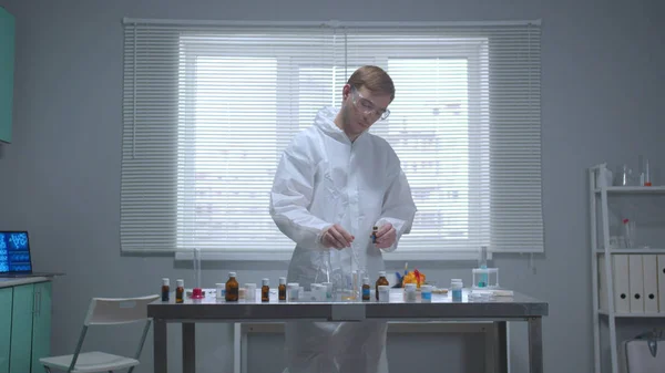 Вид спереди, человек в защитной рабочей одежде берет химикат из пробирки в лаборатории — стоковое фото