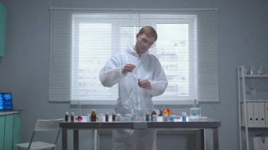 Koruyucu iş kıyafetli bir adam laboratuardaki tüpten madde alıyor.