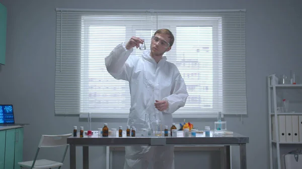 Человек в защитной рабочей одежде наливает жидкость в трубу в лаборатории — стоковое фото