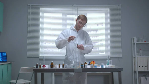 Человек в защитной рабочей одежде берет вещество из трубки в лаборатории — стоковое фото
