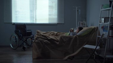 Küçük kız hastanede yatakta yatıyor, tabletle oynuyor.