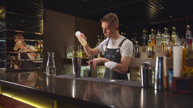 Barmen kokteyl bardağına alkol koyar ve barda buzla karıştırır.