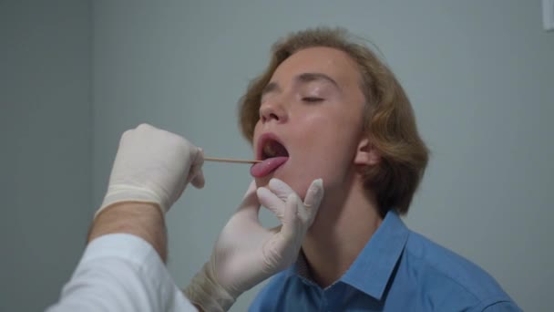 Boy sit in cabinet of hospital, doctor check his throat with stick — Stock Video