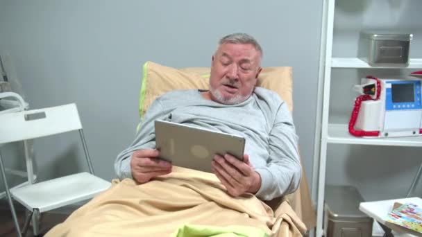 Homme allongé sur le lit et parler avec quelqu'un sur la tablette et agiter sa main — Video