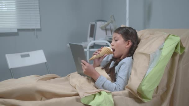 Mädchen liegen auf dem Bett, essen Eis und schauen etwas auf dem Tablet — Stockvideo