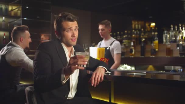 Мужчина пьет алкоголь в баре, смотрит в камеру с улыбкой. — стоковое видео