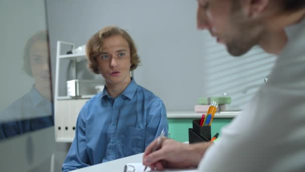 Jongen zit in de kast van het ziekenhuis en praat met een arts die schrijft — Stockvideo