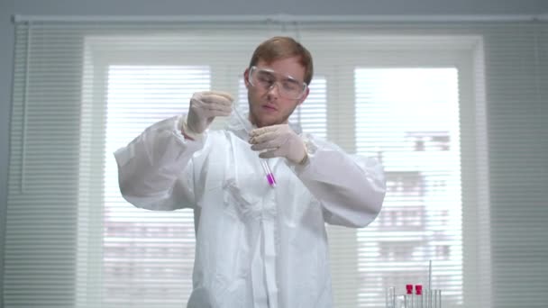 Científico en ropa de trabajo protectora vierta algo en el tubo y agítelo en el laboratorio — Vídeo de stock