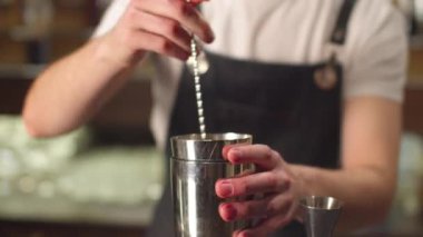 Bartender mixes alcohol and syrups in shaker, close up
