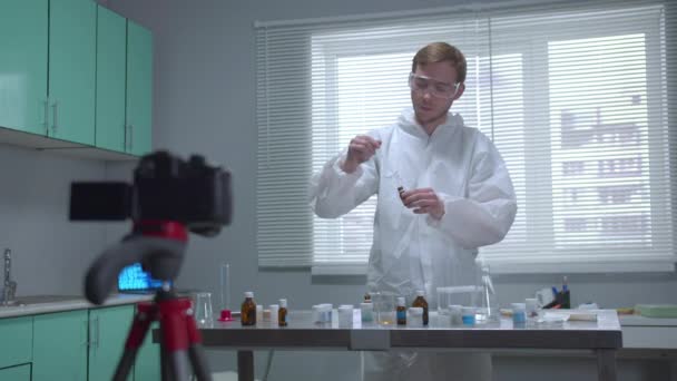 Koruyucu iş kıyafetli adam çalışmalarını laboratuvarda kameraya gösteriyor. — Stok video