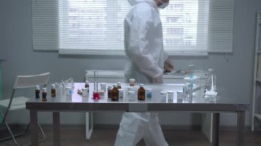 Laboratuvarda koruyucu iş kıyafeti ve maske giyen bir adam var.