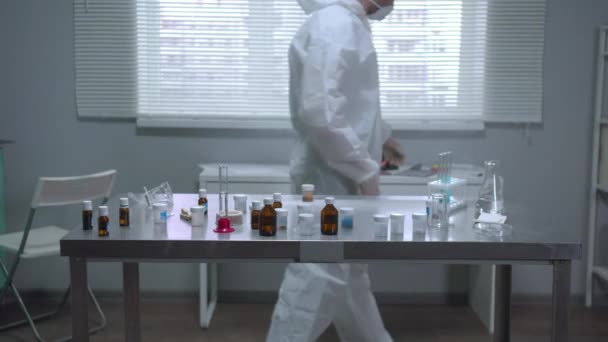 Laboratuvarda koruyucu iş kıyafeti ve maske giyen bir adam var. — Stok video
