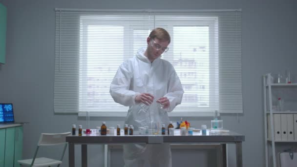 フロントビュー、保護作業服の男は、研究室でチューブに液体を注ぎます — ストック動画