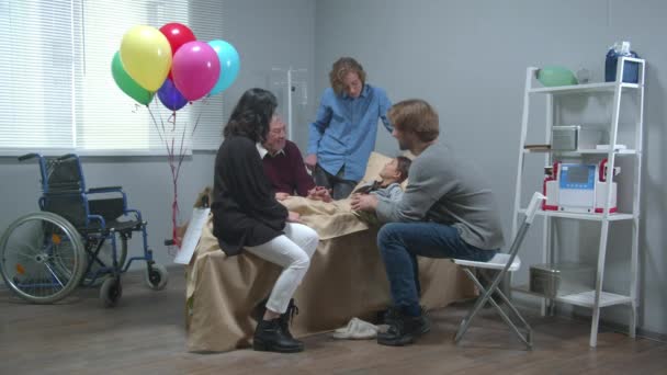 Des parents viennent rendre visite à une fille allongée sur le lit de l'hôpital et lui parlent. — Video