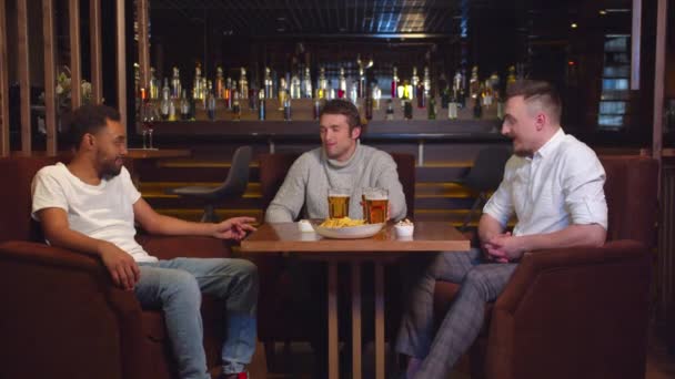 Amigos multiculturales se sientan en el bar, beben cerveza y charlan — Vídeos de Stock