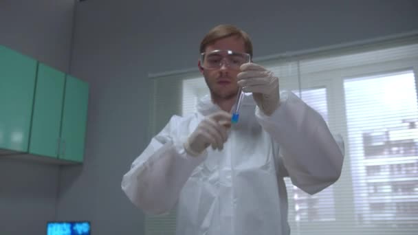 Chemik w ochronnej tubie do wytrząsania odzieży roboczej z niebieskim płynem i wysyła go do laboratorium — Wideo stockowe