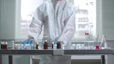 Koruyucu iş kıyafetleri ve eldivenler bilim adamı laboratuvarda kimyasallarla çalışıyor.