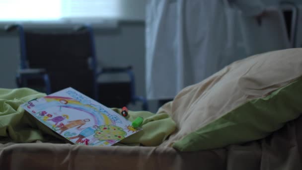 Focus on bed with drawing of child, doctor walk on the background — Stock Video