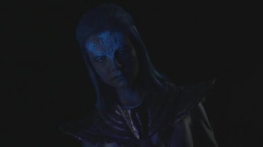 Parlayan yüzlü bir uzaylı karanlıkta kameraya bakıyor.