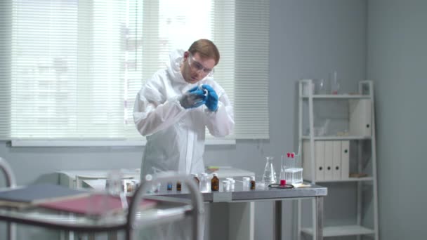 Man i skyddsarbetskläder, glasögon och medicinska handskar titta på utrustning i laboratoriet — Stockvideo