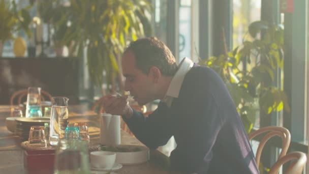 El hombre se sienta en una mesa en la cafetería y come ensalada — Vídeos de Stock