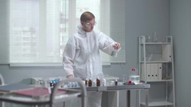 Koruyucu iş kıyafeti giyen adam laboratuarda kimyasal test tüplerini kontrol ediyor.