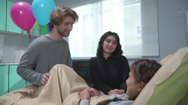 Чоловік дарує подарунок дівчині, яка лежить на ліжку в лікарні — стокове відео