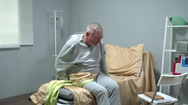 Az orvos segít az öregnek tolószékben ülni a kórházban. — Stock videók