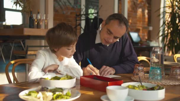 Hombre enseñar a niño a escribir en la cafetería — Vídeos de Stock