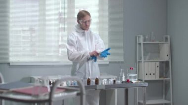 Koruyucu iş kıyafetli bir adam laboratuarda tıbbi eldiven takmış.