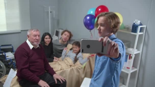 Familieleden bezoeken meisje die op het bed liggen in het ziekenhuis, jongen neemt een foto — Stockvideo