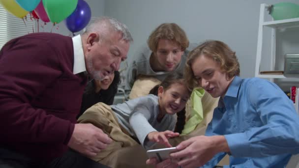 Люди відвідують дівчину в лікарні, хлопчик показує фото по телефону і всі сміються — стокове відео