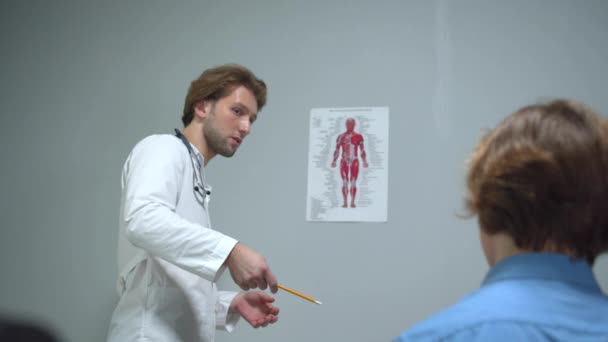 Doctor tonen foto van het menselijk lichaam om jongen en iets uit te leggen, achteraanzicht — Stockvideo