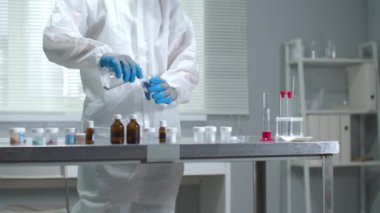 Koruyucu iş giysisi ve eldiven giyen adam laboratuarda tüpe sıvı döküyor.