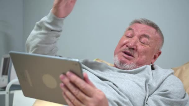 Mann liegt im Krankenhaus auf dem Bett und redet aggressiv auf Tablet — Stockvideo