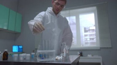 Scientist in protective workwear pour liquid in tubes in the laboratory