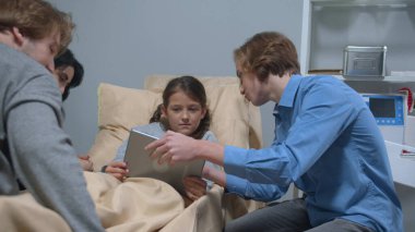 Yan görüş, oğlum tablette bir şey göster. Hastanede yatakta yatan kıza.