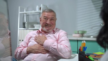 Yaşlı adam hastane kabinesinde otur ve doktorla konuş.