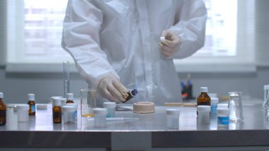 Koruyucu iş kıyafetli adam laboratuarda yanan şeyin üzerine bir şey döktü.