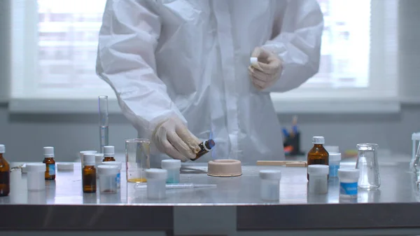 Koruyucu iş kıyafetli adam laboratuarda yanan şeyin üzerine bir şey döktü.