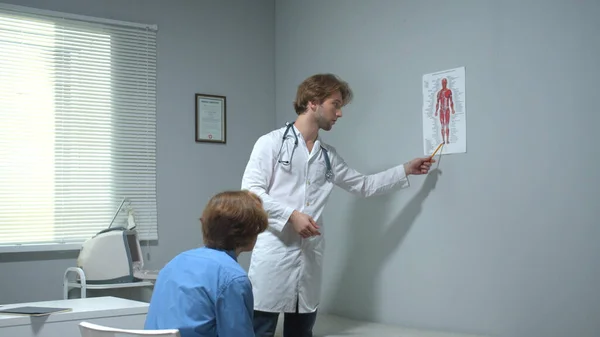 Lekarz pokaże zdjęcie ludzkiego ciała chłopcu i coś wyjaśni. — Zdjęcie stockowe