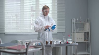 Koruyucu iş kıyafetli bir adam laboratuarda tıbbi eldiven takmış.
