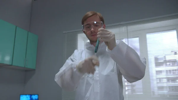 Ученый в области защитной рабочей одежды встряхнуть трубу с жидкостью и засорить ее в лаборатории — стоковое фото